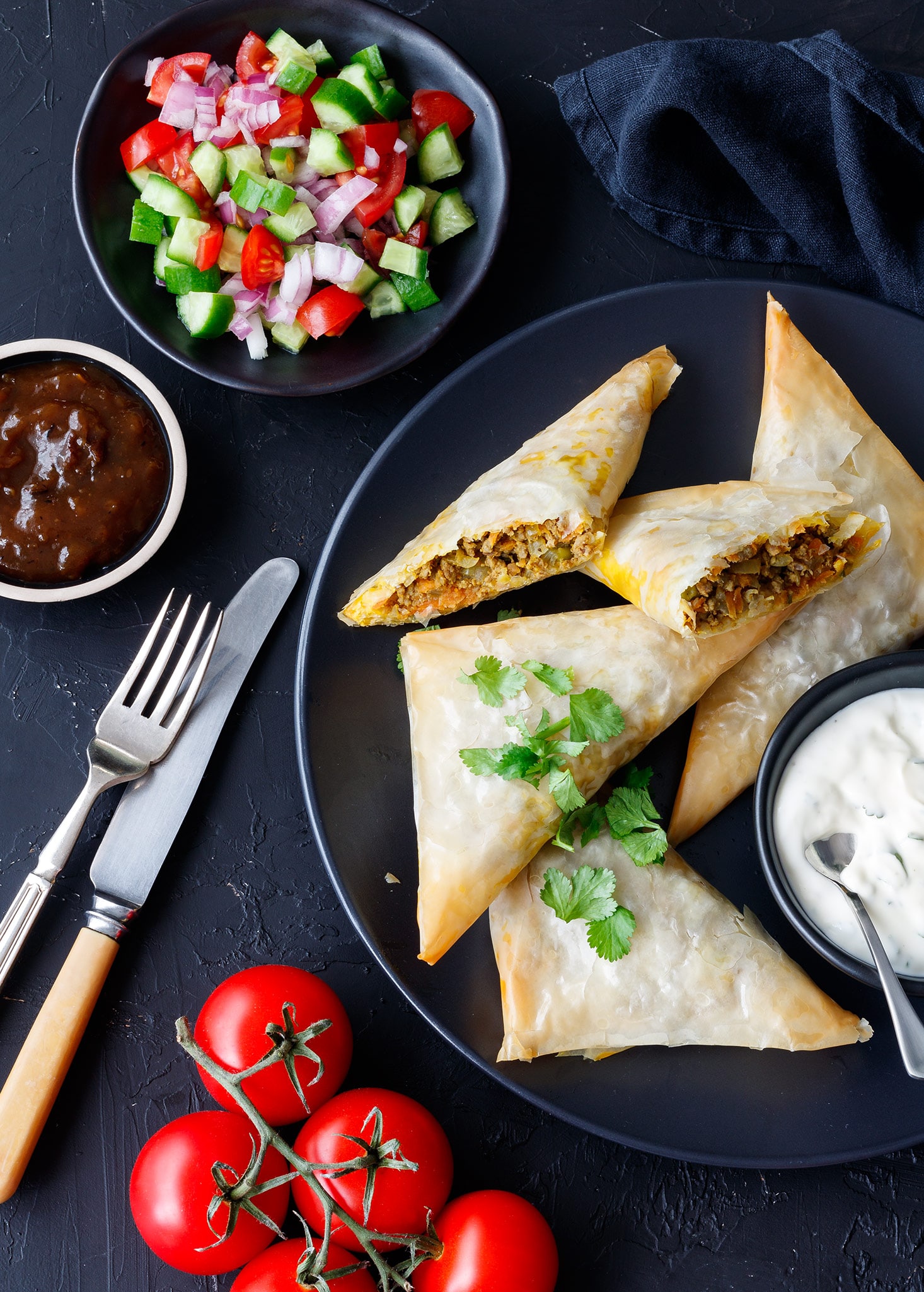 Lamb samosas on a plate with condiments.
