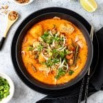 Bowl of prawn laksa with limes, fried shallots and spring onions.