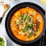 Bowl of prawn laksa with limes, fried shallots and spring onions.